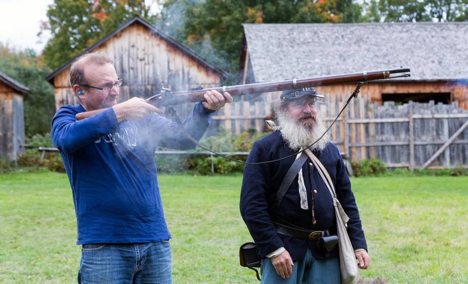 A man firing a musket with a man dressed as a Union soldier standing next to him.
