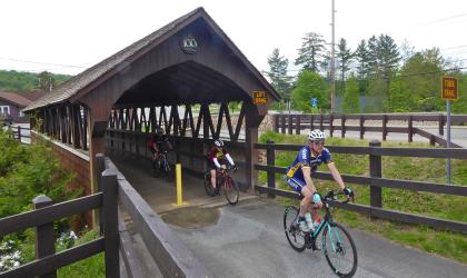 People bike over a small covered bridge