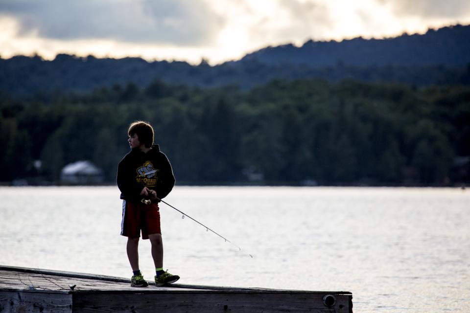 A young boy fishes off a dock in the early morning.