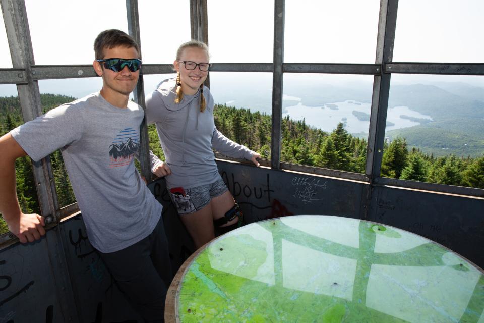 A man and woman stand inside a fire tower at the top of a mountain.