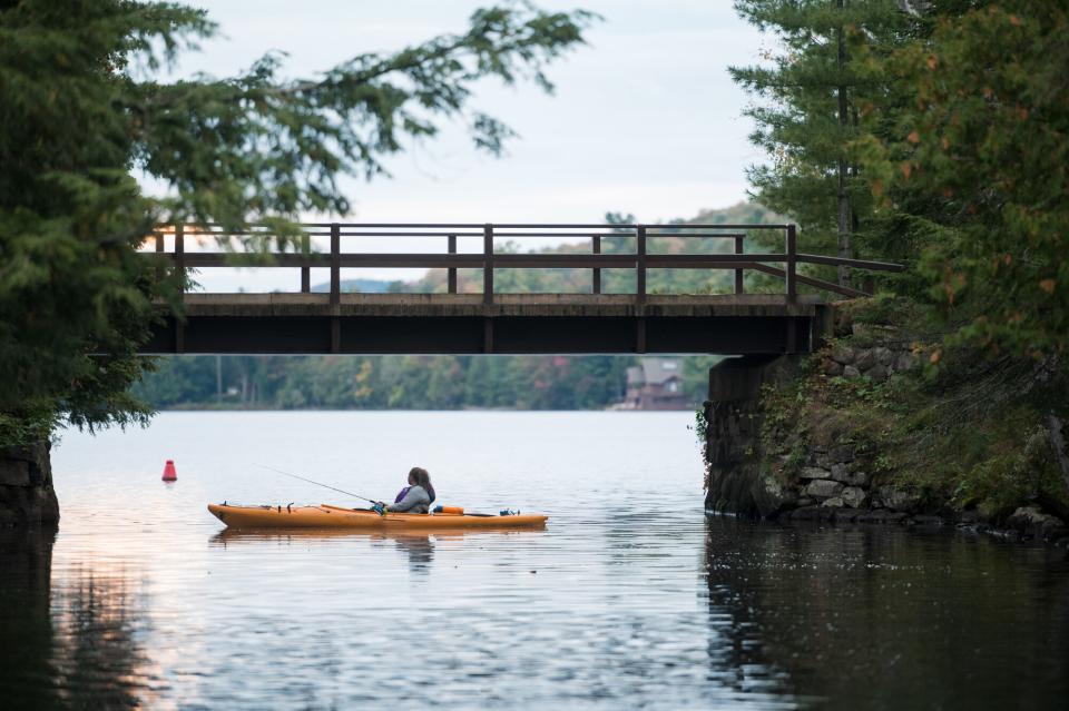 a woman fishes off of a kayak under a bridge.