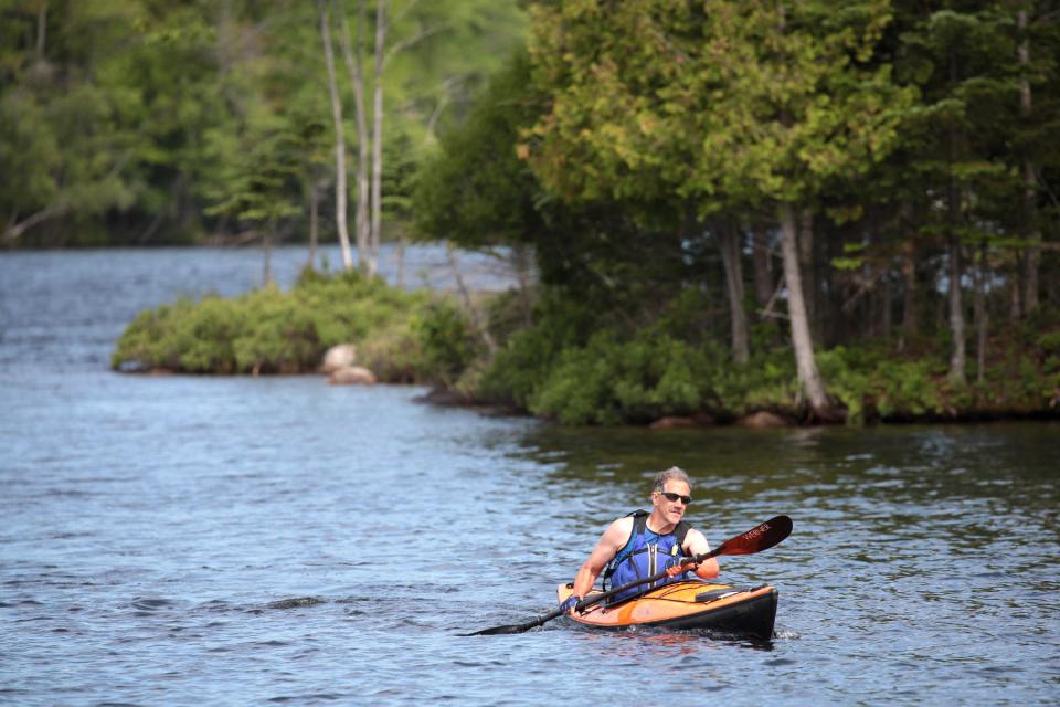 A man paddles out near the shoreline of a lake.