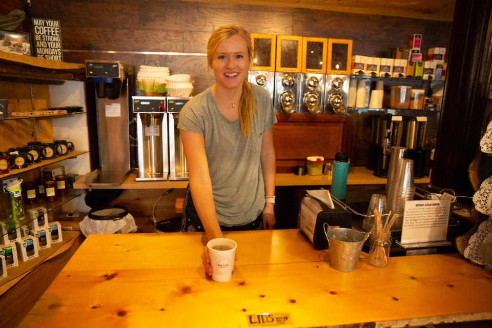 A tall blonde woman serves a cup of coffee at a coffee shop counter.