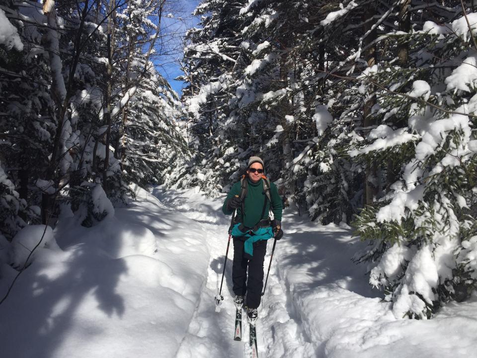 Cross-country skier on wooded trail with heavy snow