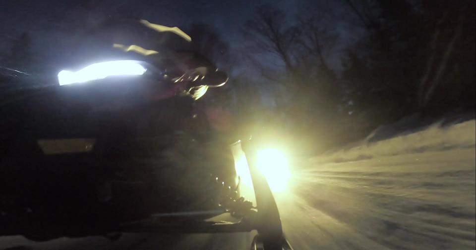 A closeup image of the headlights of a snowmobile cruising through the snow before the sun comes up.