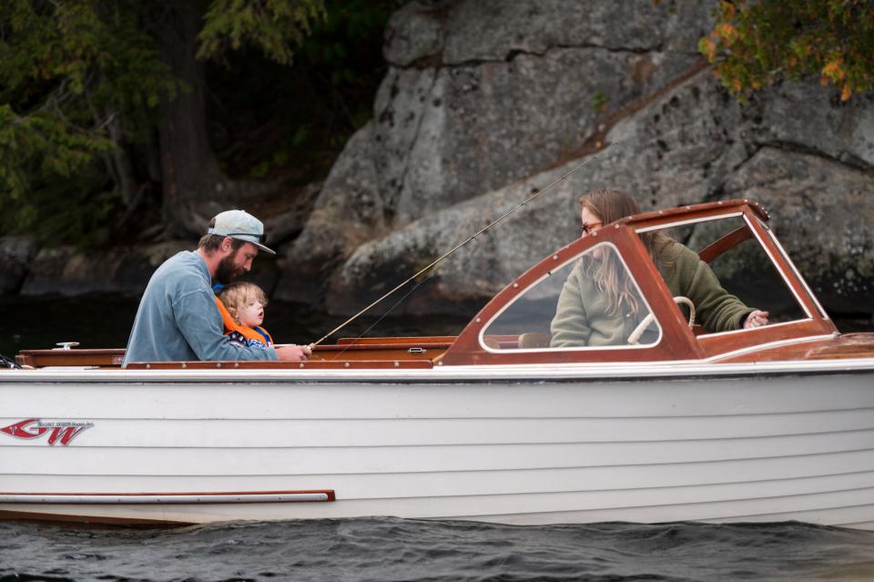 A father, mother, and young son fish from a wooden boat.
