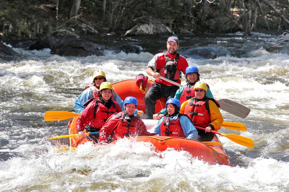 A group of people in helmets and floatation devices whitewater paddling on a turbulent river.