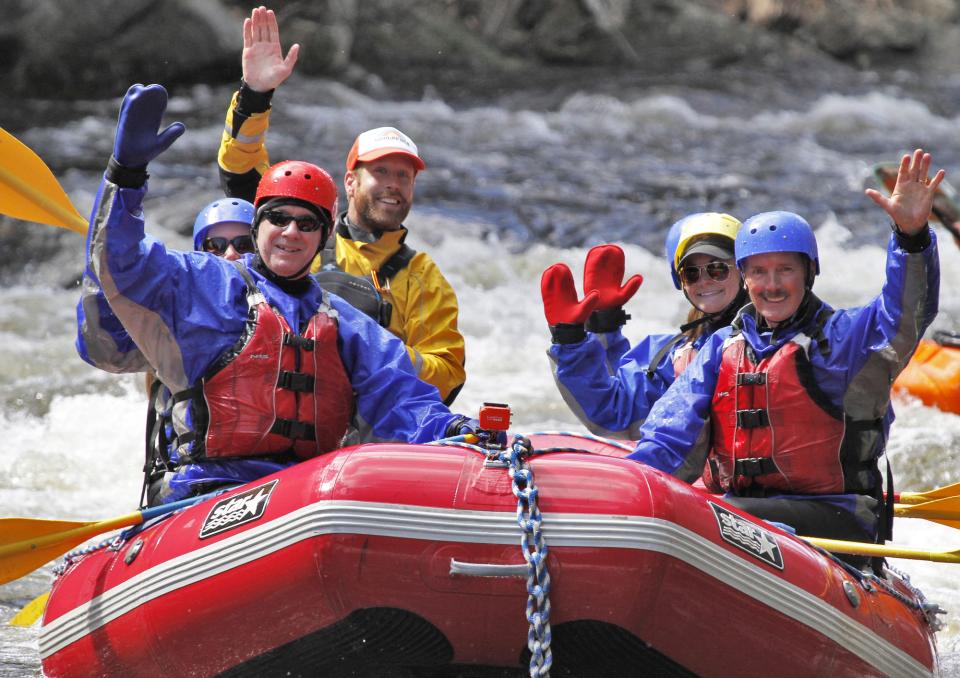 A group of people smile and wave while whitewater rafting