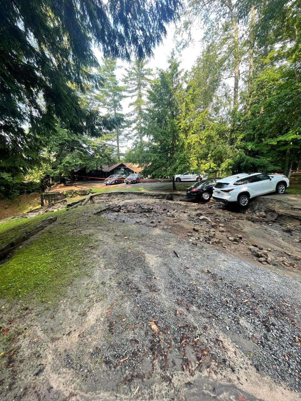 A car leans off a cliff of dirt from a washed out parking area.