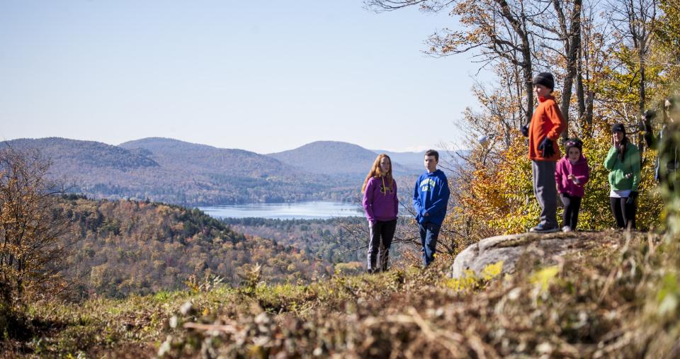 A family wearing brightly colored clothing stands on top of Oak Mountain in Speculator in the fall