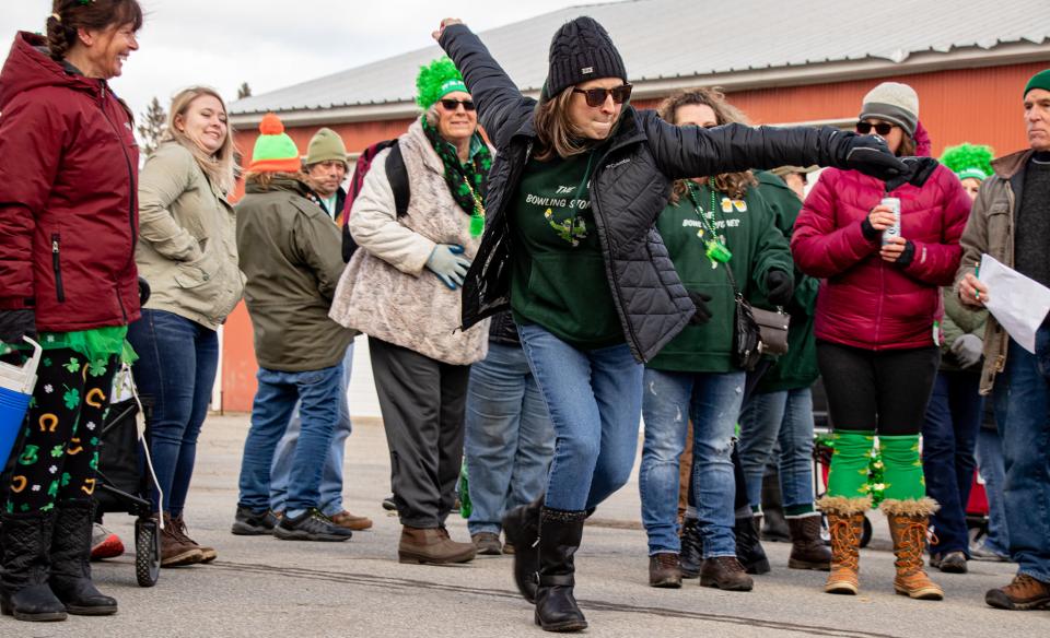 a group of people dressed for St Patrick's Day watching a woman as she takes her turn at Irish road bowling.