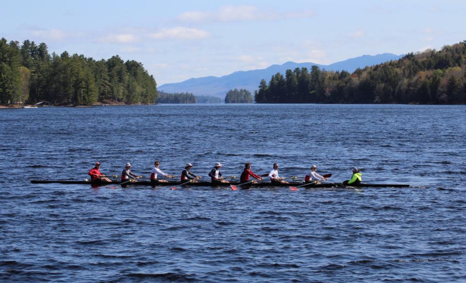 A crew of men on a rowing team rowing their boat on a lake