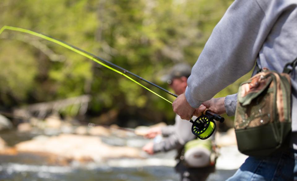 a close up of the fly fishing rod a man is holding while fly fishing with another man fishing in the background