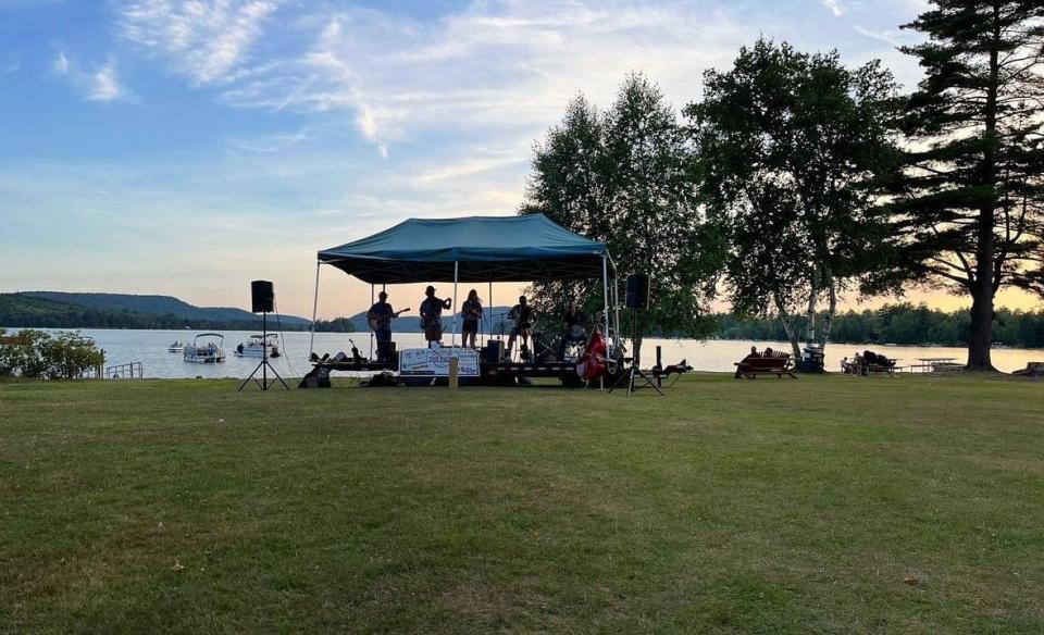 A band playing music under a canopy with the view of Lake Pleasant in the background with the sun setting