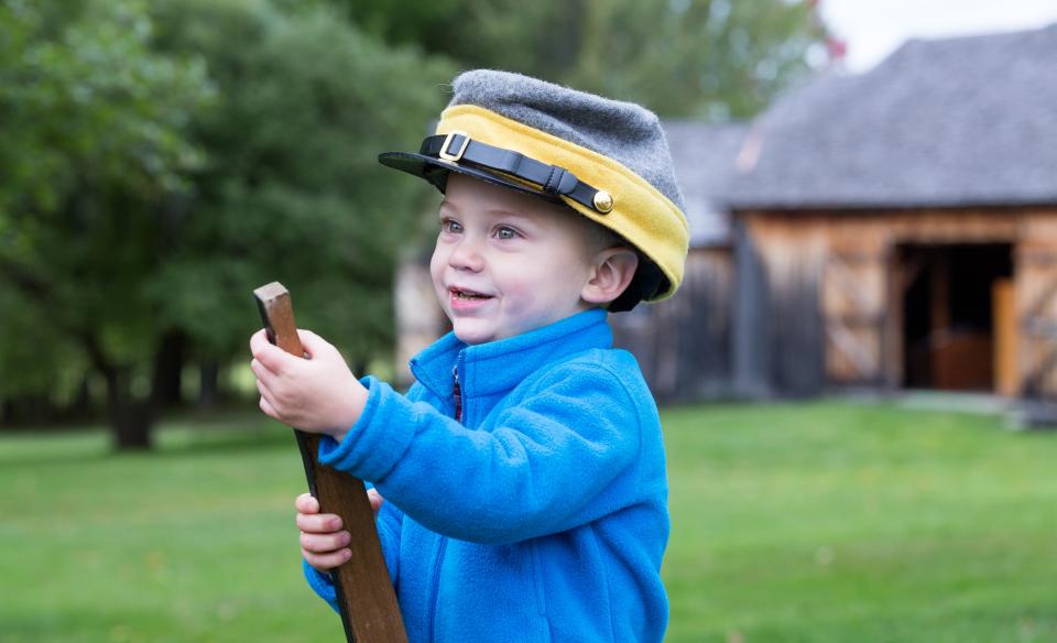 A small boy holding a wooden gun wearing a Confederate soldier's cap