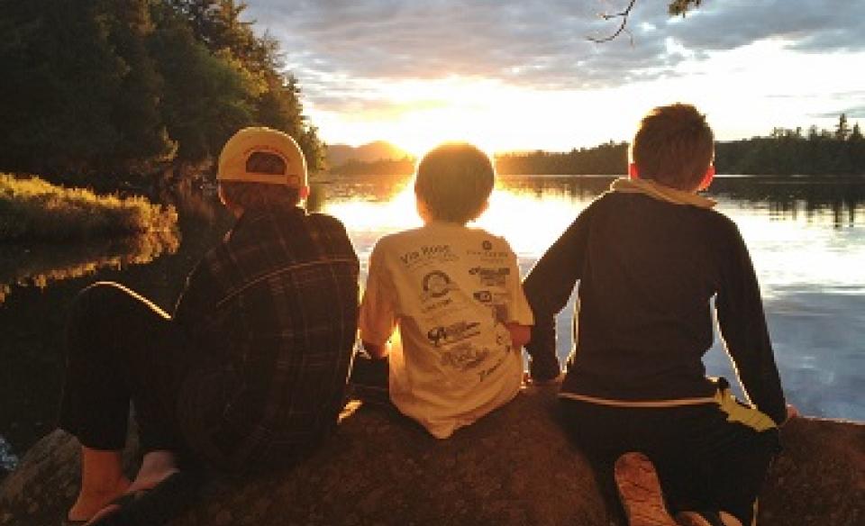 Three boys look out at the sunset over Forked Lake