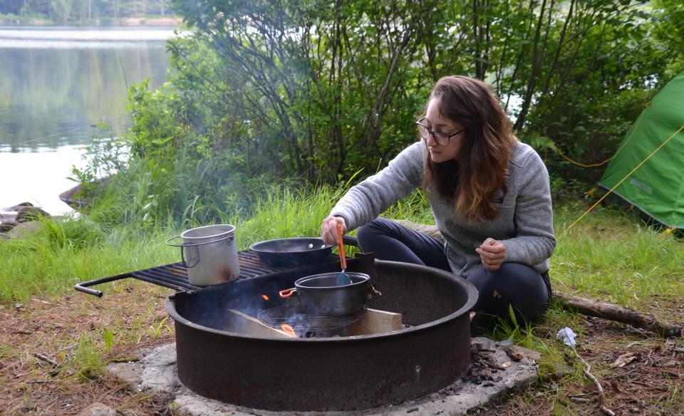 A woman cooks over a campfire at Forked Lake Campground