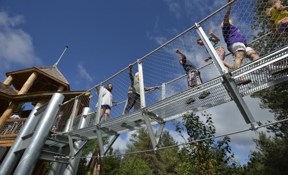 People crossing a suspended metal walkway between large wooden structures at The Wild Center in Tupper Lake NY