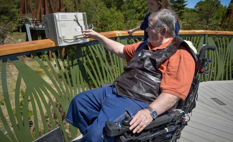 A man who uses a wheelchair stops along The Wild Walk to read a plaque