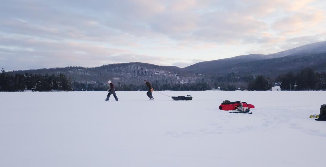 Two people pull a sled over the ice
