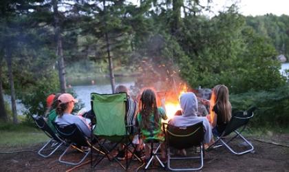 A family sits in camp chairs around a campfire at Forked Lake Campground