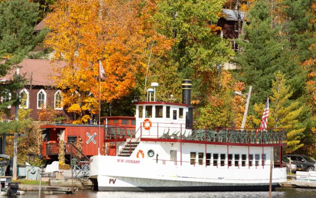 A replica steamboat sits at a dock in front of colorful fall foliage.
