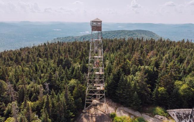 An aerial shot of a fire tower standing above a mountain.
