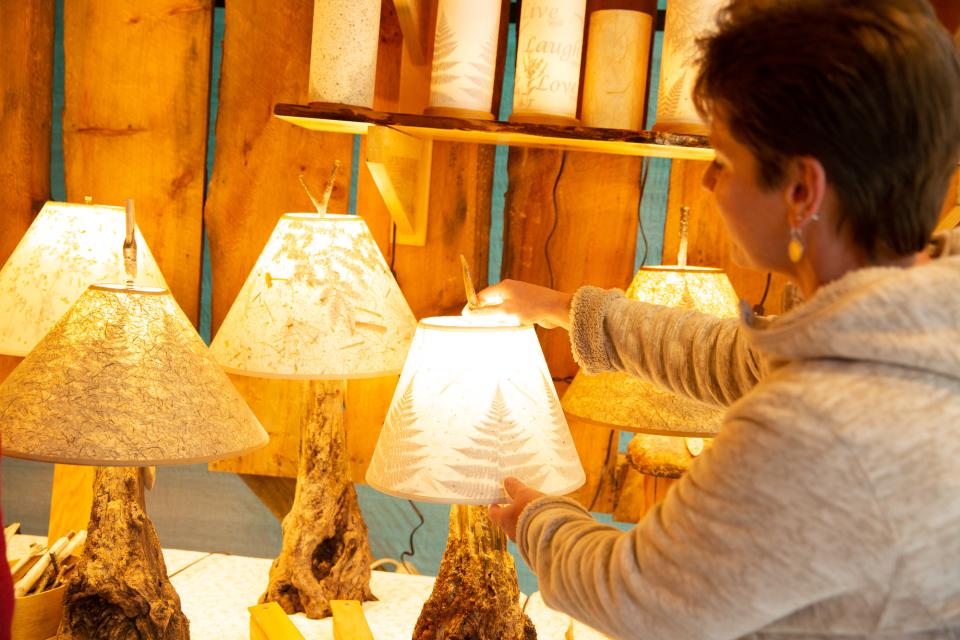 A woman touches a lamp on display of rustic wooden lamps.