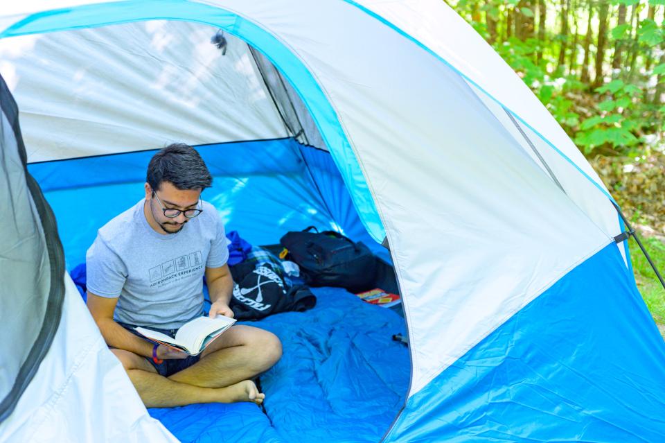 A man reads a book inside of a blue tent in a campground in the Adirondacks.