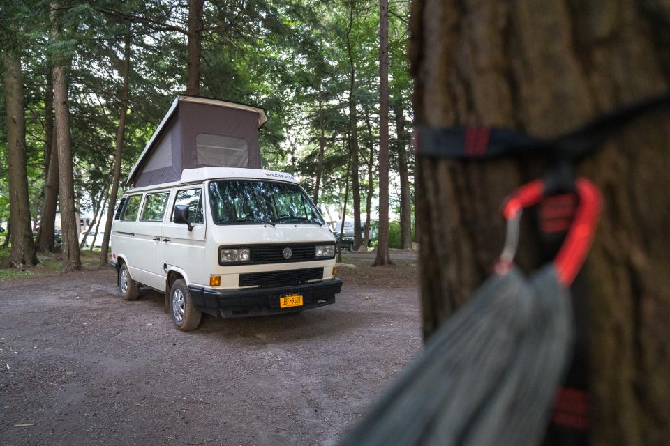 A camper van with roof popped up sits among trees at a wooded campsite.