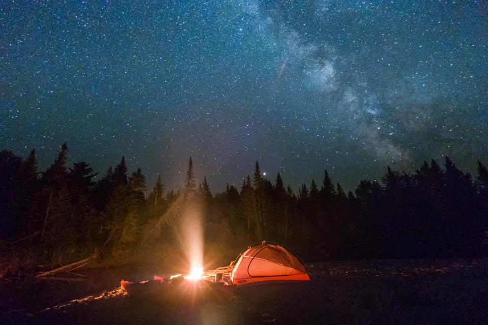 A night sky bright with stars above a campsite with tent and fire.