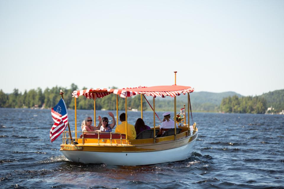 A classic wooden motorboat with a striped awning carries boaters on a tour on a lake.