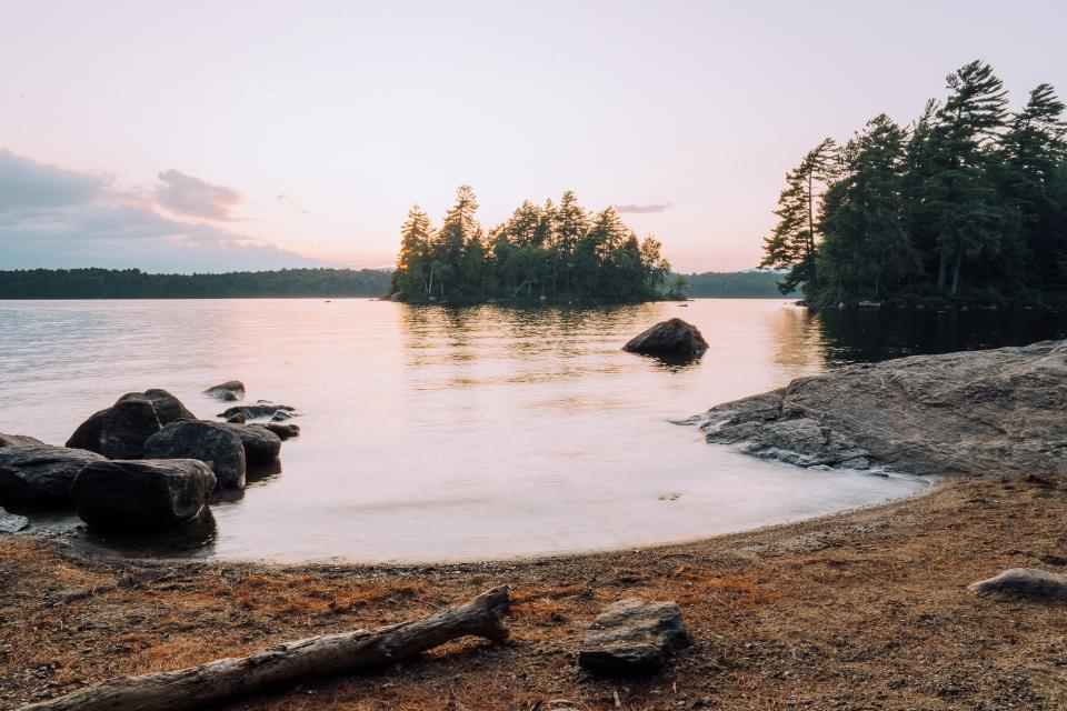 A sandy beach at sunset with a small wooded island in the foreground.