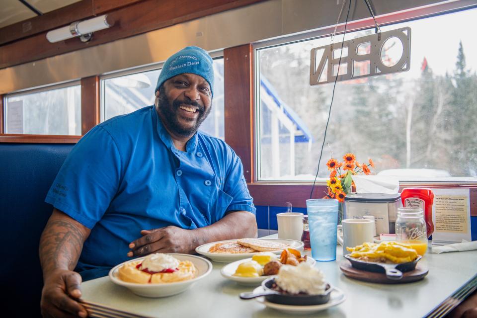 A chef smiles sitting by his creations at a diner.