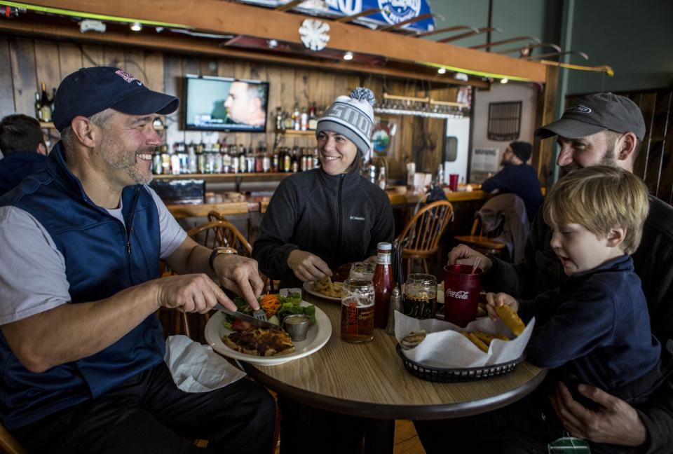 A family sits around a table eating a meal in warm ski clothing.