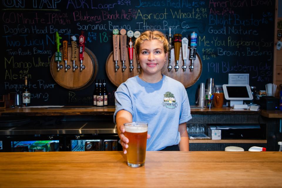a woman holds a pint of beer at a bar.