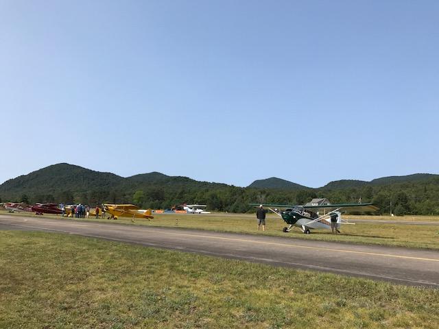 people stand next to small prop-planes in a field.