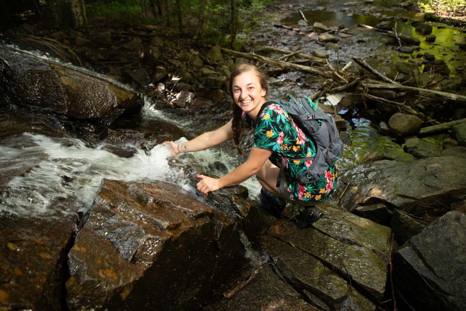 A young woman climbing a rocky waterfall in a forest smiles.