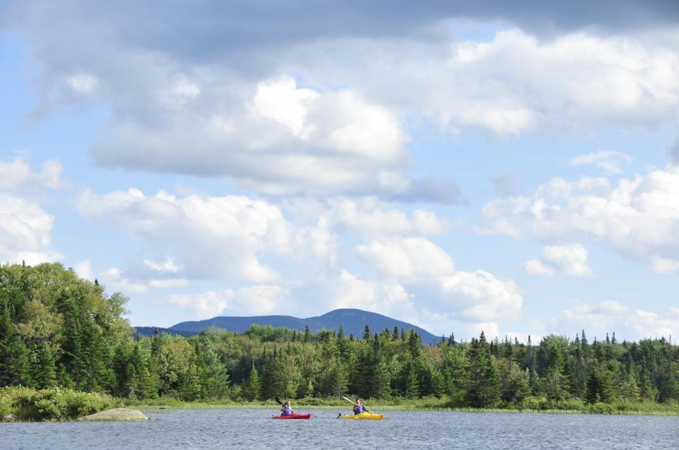 Two people in kayaks on a lake with forest and mountains in the background.