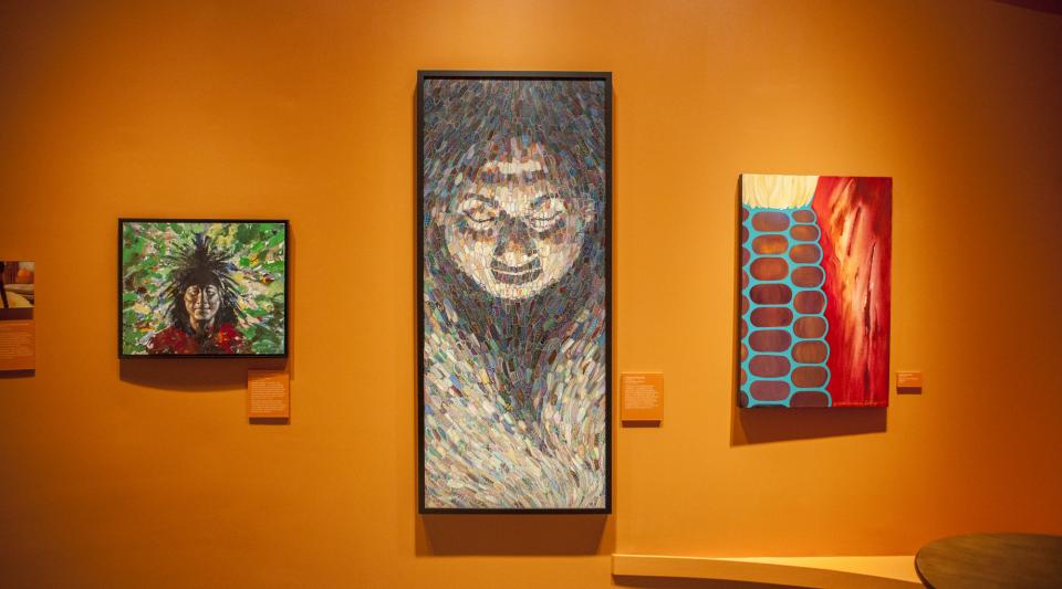 Three vertically-oriented paintings depicting modern Indigenous American art hang on an orange wall.