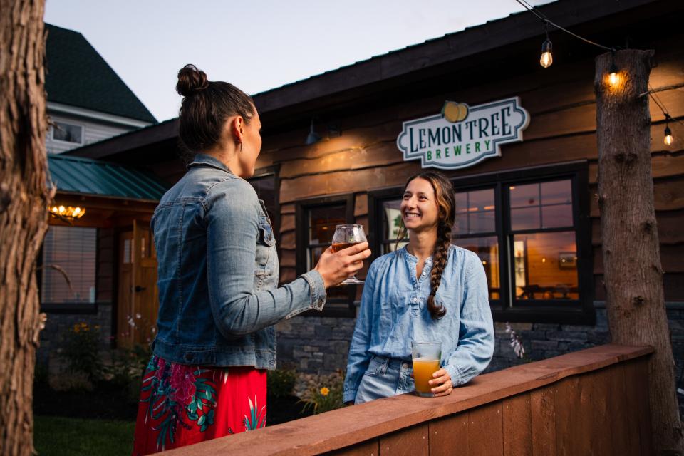 Two women stand on a wooden deck at a rustic brewery in early twilight.