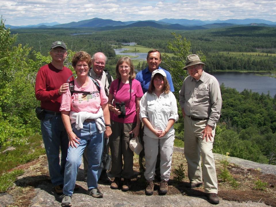 A group of birders on a mountain summit with a river and mountains in the background.