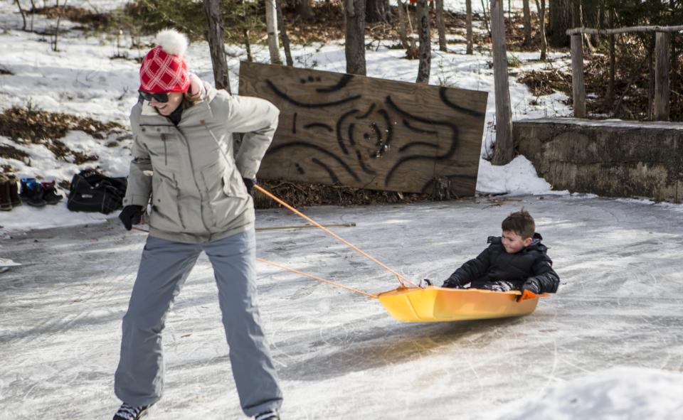Woman skating on a pond and pulling kids in a sled