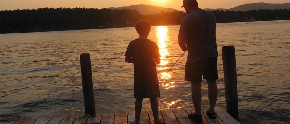 Boy and father fishing from dock at sunset