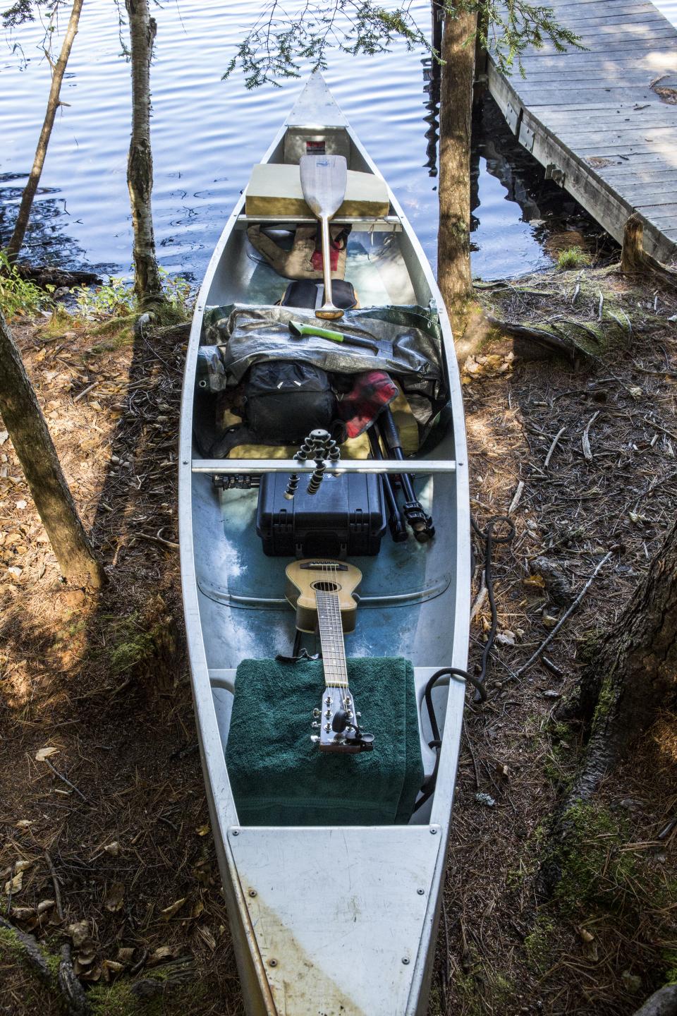 A canoe loaded with camping supplies and a guitar.