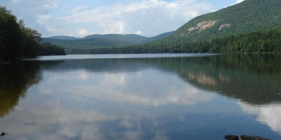 A peaceful view across Tirrell Pond with cliffs on one side and rolling hills in the distance.