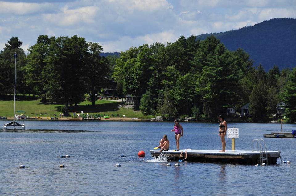 Swimmers stand on a floating dock in Blue Mountain Lake
