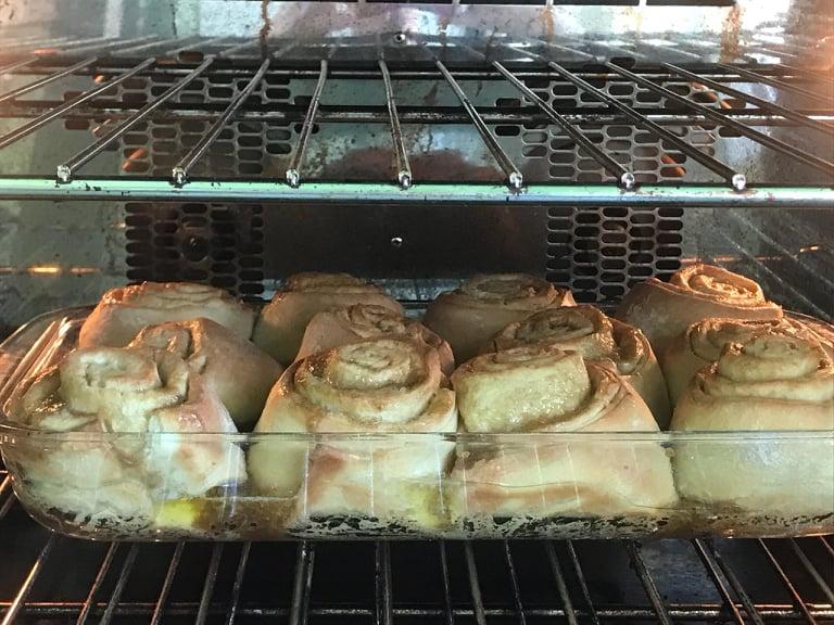 Cinnamon buns baking in a glass tray in the oven