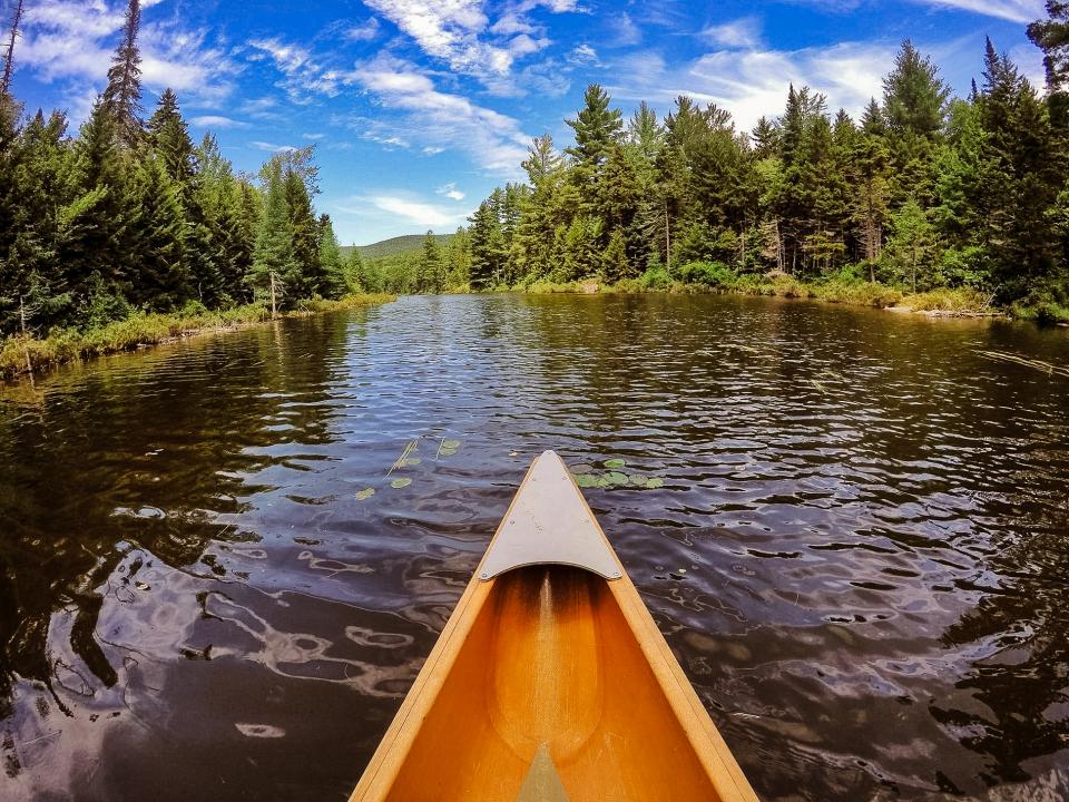 A canoe points toward an Adirondack pond surrounded by a forested shoreline.