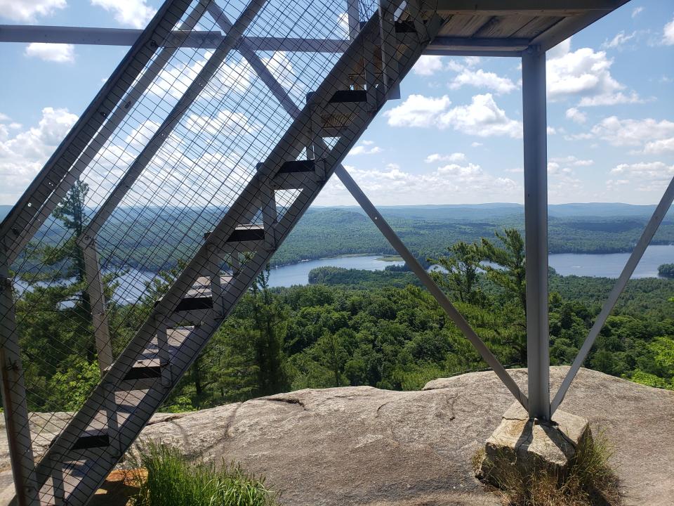 The view from a fire tower summit, with the metal staircase and lake below.